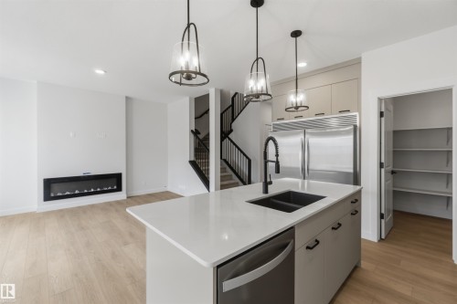 Open-concept living area featuring a modern kitchen island with an integrated sink and dishwasher, two pendant light fixtures, and stainless steel appliances - 5872 Raven Crescent Nw, Edmonton, AB - Indoor Photo Showing Kitchen With Double Sink With Upgraded Kitchen
