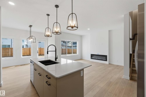 Open-concept living space featuring a central kitchen island with a dark sink and matte black faucet, integrated dishwasher, and pendant lighting - 5872 Raven Crescent Nw, Edmonton, AB - Indoor Photo Showing Kitchen With Double Sink With Upgraded Kitchen