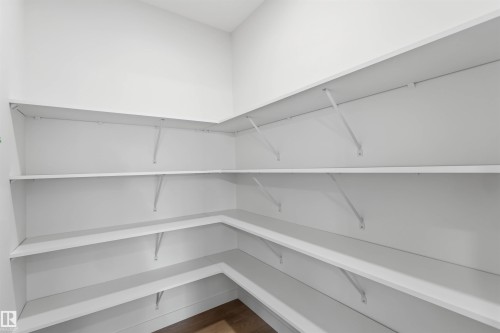 Spacious corner pantry featuring multiple levels of white shelving, white walls, and wood-finish flooring - 5872 Raven Crescent Nw, Edmonton, AB - Indoor With Storage