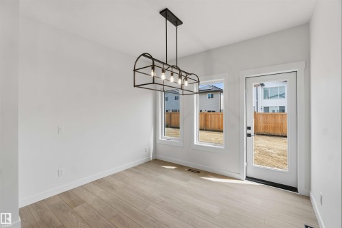 Open-concept interior featuring light wood-finish flooring, white walls, and a contemporary black linear chandelier - 5872 Raven Crescent Nw, Edmonton, AB - Indoor Photo Showing Other Room