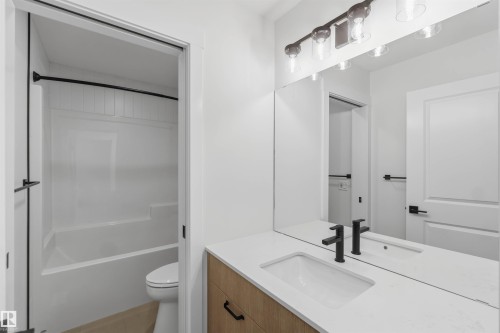 Bathroom featuring a wood-finish vanity with a white countertop and integrated sink, matte black faucet, and frameless mirror - 5872 Raven Crescent Nw, Edmonton, AB - Indoor Photo Showing Bathroom