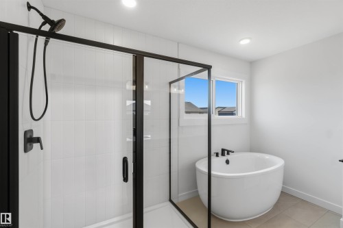 Contemporary bathroom featuring a freestanding round soaking tub, a walk-in shower with black-framed glass enclosure, matte black fixtures, and white vertical subway tile - 5872 Raven Crescent Nw, Edmonton, AB - Indoor Photo Showing Bathroom