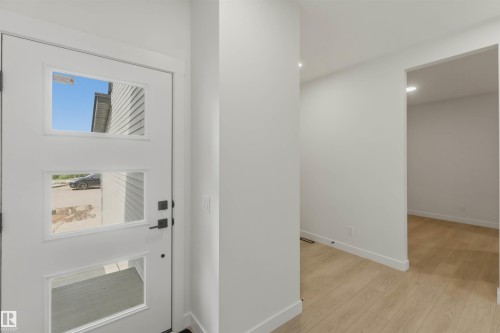Modern entryway featuring a white entry door with three rectangular lites, black hardware, and light wood-finish flooring - 5872 Raven Crescent Nw, Edmonton, AB - Indoor Photo Showing Other Room