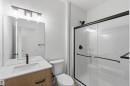 Contemporary bathroom featuring a light wood-finish vanity with a white countertop and integrated sink, a large frameless mirror, a shower enclosure with black hardware and clear glass doors, a white toilet, and white vertical paneled wall accents - 5872 Raven Crescent Nw, Edmonton, AB  - Indoor Photo Showing Bathroom 
