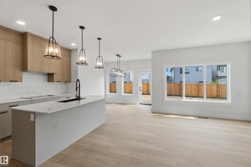 Modern kitchen featuring a large island with sink, neutral cabinetry, subway tile backsplash, and light wood-finish flooring - 5872 Raven Crescent Nw, Edmonton, AB - Indoor Photo Showing Kitchen With Upgraded Kitchen