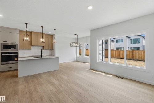 Modern kitchen featuring light wood-finish flooring, a kitchen island with sink, and stainless steel appliances - 5872 Raven Crescent Nw, Edmonton, AB - Indoor Photo Showing Kitchen