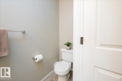 Bathroom featuring a white toilet with a lidded tank, beige wall paint, a chrome towel bar, and a chrome toilet paper holder - 