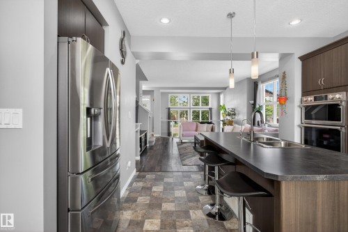 Kitchen featuring a stainless steel French door refrigerator, dark wood-finish cabinetry, a large center island with integrated sink, pendant lighting, and patterned floor tiles - 9847 220 Street Nw, Edmonton, AB - Indoor Photo Showing Kitchen With Double Sink With Upgraded Kitchen