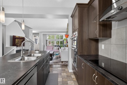 Kitchen featuring dark wood-finish cabinetry, stainless steel double wall oven, and a built-in cooktop with a stainless steel range hood - 9847 220 Street Nw, Edmonton, AB - Indoor Photo Showing Kitchen With Double Sink