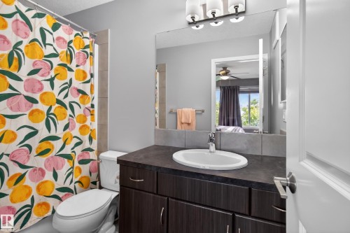 Vanity with a dark countertop and integrated sink, complemented by a large wall mirror and a three-light fixture - 9847 220 Street Nw, Edmonton, AB - Indoor Photo Showing Bathroom