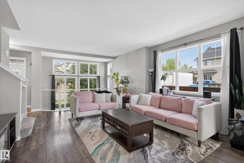 Living area featuring large windows, wood-finish flooring, light gray walls, and white trim - 9847 220 Street Nw, Edmonton, AB - Indoor Photo Showing Living Room