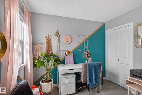 Dedicated office space featuring a white desk with integrated drawer storage, a large window with sheer drapes, a closet with bi-fold doors, and neutral carpeting - 9847 220 Street Nw, Edmonton, AB - Indoor Photo Showing Other Room