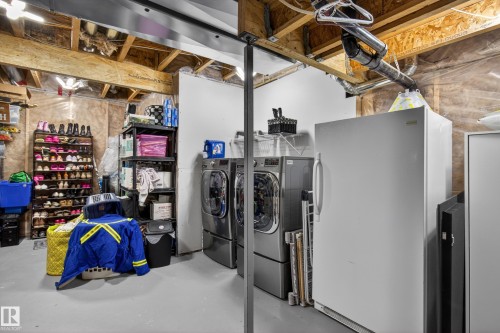 Utility area featuring exposed wood joists, a concrete floor, and built-in washing machines - 9847 220 Street Nw, Edmonton, AB - Indoor Photo Showing Laundry Room