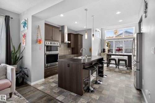 Kitchen featuring a central island with countertop seating, stainless steel appliances including double ovens and a range hood, dark wood-finish cabinetry, and recessed lighting - 9847 220 Street Nw, Edmonton, AB - Indoor Photo Showing Kitchen With Upgraded Kitchen