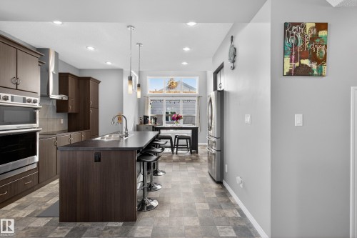 Modern kitchen featuring dark wood-finish cabinetry, stainless steel appliances, a center island with bar seating, pendant lighting, and tiled flooring - 9847 220 Street Nw, Edmonton, AB - Indoor Photo Showing Kitchen