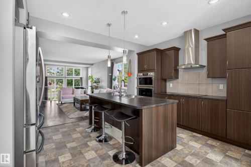 Modern kitchen featuring dark wood-finish cabinetry, a large center island with seating, stainless steel appliances, and recessed lighting - 9847 220 Street Nw, Edmonton, AB - Indoor Photo Showing Kitchen With Upgraded Kitchen