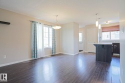 Open-concept living area with dark wood-finish flooring, a contemporary pendant light fixture, and a large window providing natural light - 