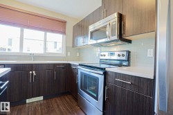 Contemporary kitchen featuring dark wood-finish cabinetry, stainless steel appliances, light countertops, and a full-height tile backsplash - 