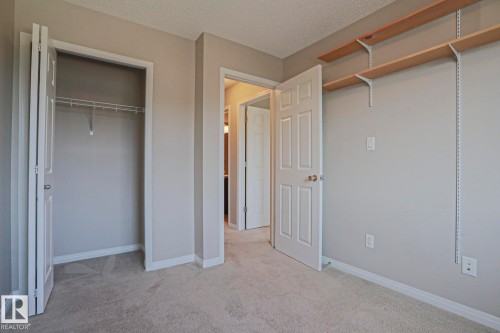 Carpeted room featuring light gray wall paint, white trim, a bi-fold closet with wire shelving, and adjustable wall-mounted shelving - 489 Orchards Boulevard Sw, Edmonton, AB - Indoor Photo Showing Other Room