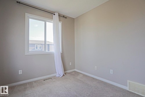 Neutral tone wall paint with white trim, carpeting, and a window with white casing - 489 Orchards Boulevard Sw, Edmonton, AB - Indoor Photo Showing Other Room