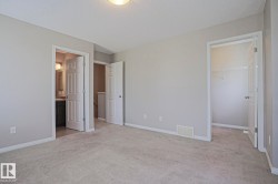 Carpeted room with light neutral wall paint, featuring a standard closet with wire shelving and a vanity area with a dark cabinet and wall-mounted light fixture - 