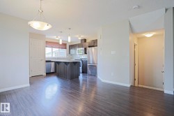 Open-concept living space featuring wood-finish flooring, a contemporary kitchen, stainless steel appliances, dark wood-finish cabinetry, and a central island with a light-colored countertop - 