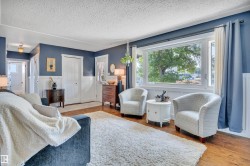 Living area featuring wood-finish flooring, white wainscoting, and large windows with outdoor scenery - 