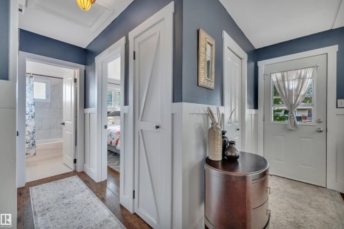 Hallway with dark wood-finish flooring, half-wall wainscoting, a white paneled door, and a decorative ceiling light fixture - 5302 52 Ave, Wetaskiwin, AB - Indoor Photo Showing Other Room