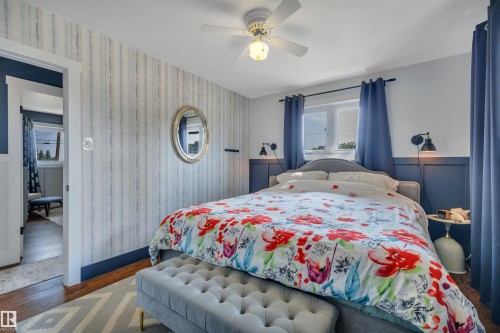 Bedroom featuring wood-finish flooring, a ceiling fan with integrated lighting, and a window with dark blue curtains - 5302 52 Ave, Wetaskiwin, AB - Indoor Photo Showing Bedroom