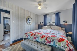 Bedroom featuring wood-finish flooring, a ceiling fan with integrated lighting, and a window with dark blue curtains - 