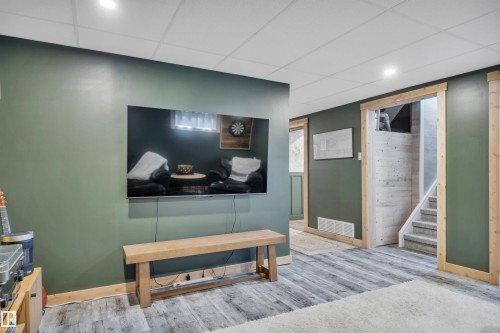 Spacious interior room featuring dark green walls, wood-finish flooring, and a drop ceiling with recessed lighting - 5302 52 Ave, Wetaskiwin, AB - Indoor