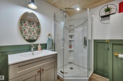 Bathroom featuring a corner shower enclosure, a vanity with an integrated sink, a gold-framed oval mirror, and wood-finish flooring - 