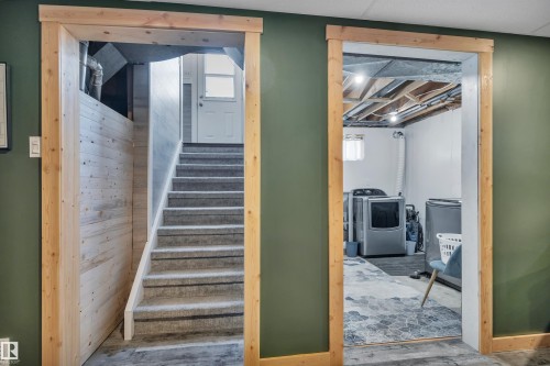 Stairwell with carpeted treads and natural wood trim, complemented by a laundry area featuring exposed ceiling joists and concrete flooring - 5302 52 Ave, Wetaskiwin, AB - Indoor Photo Showing Other Room