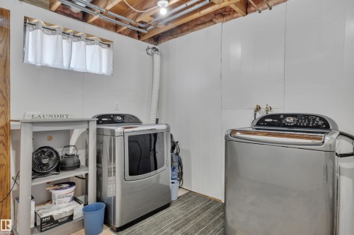 Dedicated laundry area featuring white paneled walls, exposed ceiling joists, and a window with privacy curtains - 5302 52 Ave, Wetaskiwin, AB - Indoor Photo Showing Laundry Room