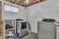 Dedicated laundry area featuring white paneled walls, exposed ceiling joists, and a window with privacy curtains - 