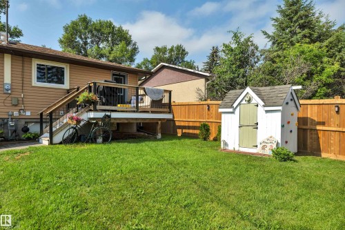 Spacious backyard featuring a low-maintenance wooden deck with dark railings, a manicured lawn, a white storage shed with a light green door and climbing holds, and a newly installed privacy fence with exterior lighting - 5302 52 Ave, Wetaskiwin, AB - Outdoor With Deck Patio Veranda