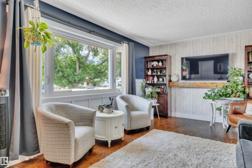 Living area featuring a large picture window, dark wood-finish flooring, and white textured wall paneling - 5302 52 Ave, Wetaskiwin, AB - Indoor Photo Showing Living Room