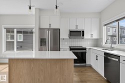 Contemporary kitchen featuring a light wood-finish island, white cabinetry, stainless steel appliances, and wood-finish flooring - 