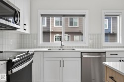 Bright kitchen featuring white cabinetry, a stainless steel sink, modern tile backsplash, and white countertops - 