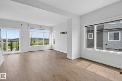 Spacious room featuring wood-finish flooring, ample natural light, a sliding glass door to a balcony with black railings, and multiple large windows - 