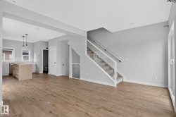 Open-concept living area featuring wood-finish flooring, a modern kitchen island with pendant lighting, a carpeted staircase with glass railing, and a sliding glass door - 