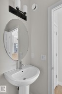 Pedestal sink with chrome faucet, complemented by a round mirror and a black vanity light fixture - 