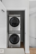 Dedicated laundry closet featuring a stacked stainless steel washer and dryer, wood-finish flooring, and a paneled door - 