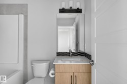 Bathroom featuring a light wood-finish vanity with a white countertop and undermount sink, complemented by a black penny tile backsplash - 