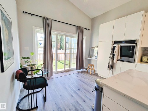 Kitchen area featuring vaulted ceilings, light wood-finish flooring, a built-in oven, white cabinetry, and sliding glass doors opening to the backyard - 215 Peter Close, Edmonton, AB - Indoor Photo Showing Other Room