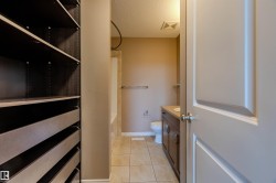 Walk-in closet featuring built-in shelving and drawers, with an adjacent bathroom displaying a dark wood-finish vanity, light-toned countertop, and tile flooring - 