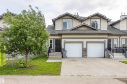 Townhome exterior featuring light-colored siding with dark trim, stone accents, two white garage doors, a paved driveway, and a front entry with steps - 