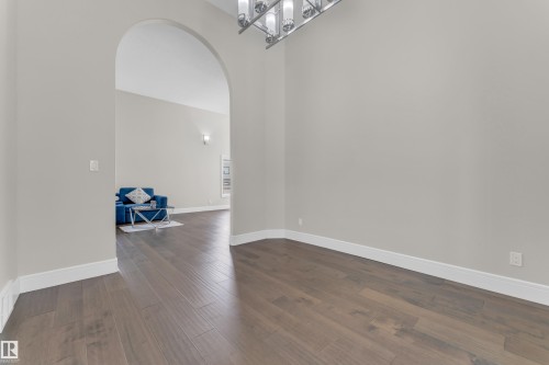 Spacious interior featuring wood-finish flooring, a contemporary chandelier, an arched doorway, and light gray walls with white baseboards - 4506 49 Avenue, Beaumont, AB - Indoor Photo Showing Other Room