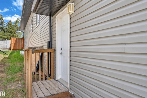 Light grey horizontal siding exterior with a white entry door, a small wooden deck, and an overhead light fixture - 4506 49 Avenue, Beaumont, AB - Outdoor