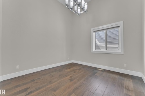 Spacious room featuring wood-finish flooring, a large window with white trim, and a modern chandelier - 4506 49 Avenue, Beaumont, AB - Indoor Photo Showing Other Room